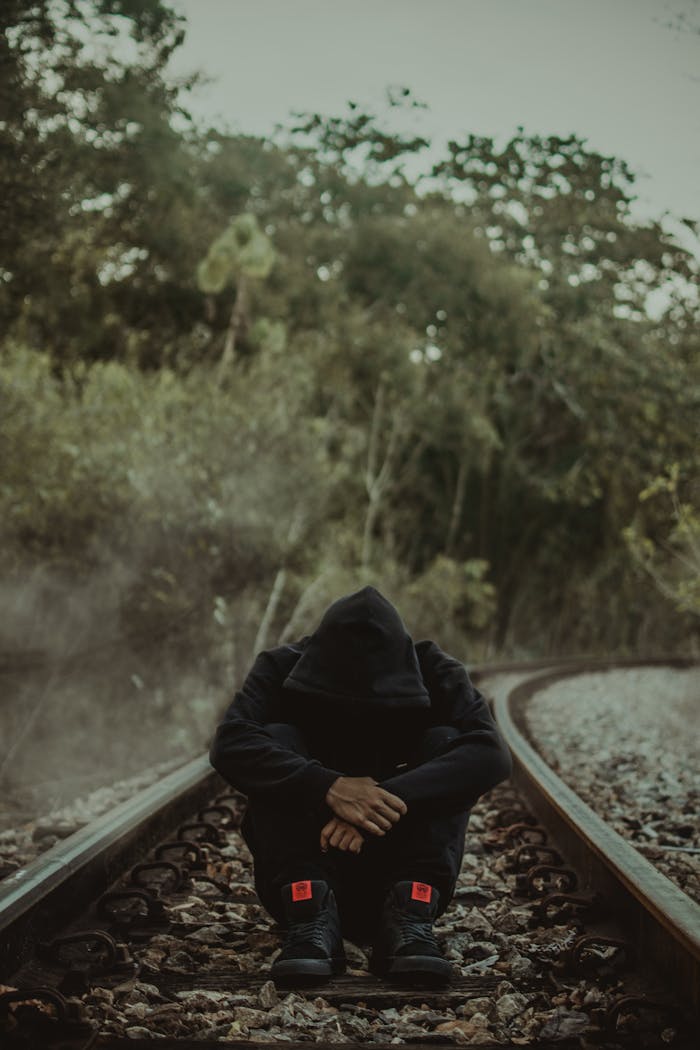 portfolio-07 A person in a hoodie sits on empty train tracks, surrounded by nature.