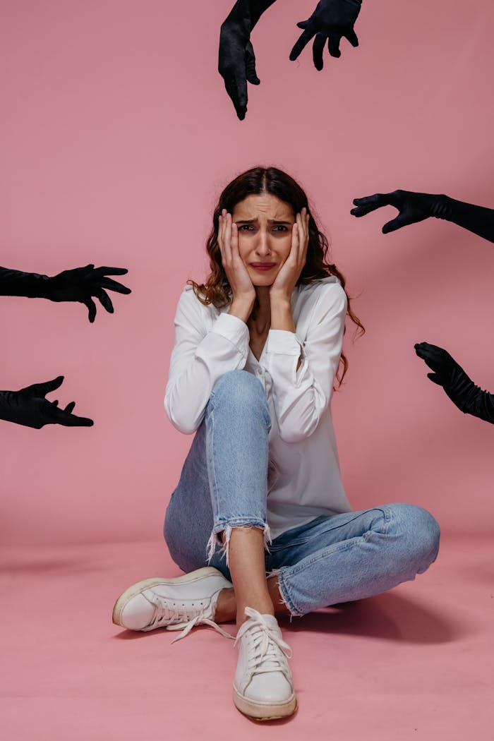 portfolio-06 A woman looks anxious and stressed, sitting against a pink backdrop with hands reaching towards her.